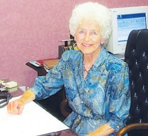 Treasure: a woman in a blue dress sitting at a desk smiling at the camera