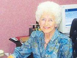 Treasure: a woman in a blue dress sitting at a desk smiling at the camera