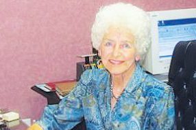 Treasure: a woman in a blue dress sitting at a desk smiling at the camera